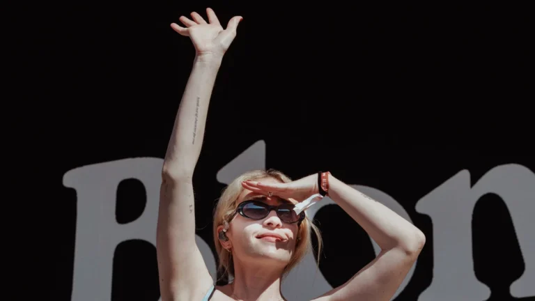 Sabrina Teitelbaum of Blondshell on stage with an arm raised in front of the band's backdrop