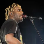 Myles Smith singing into a microphone on stage with a guitar