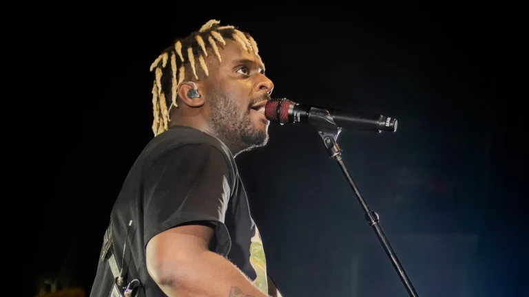 Myles Smith singing into a microphone on stage with a guitar